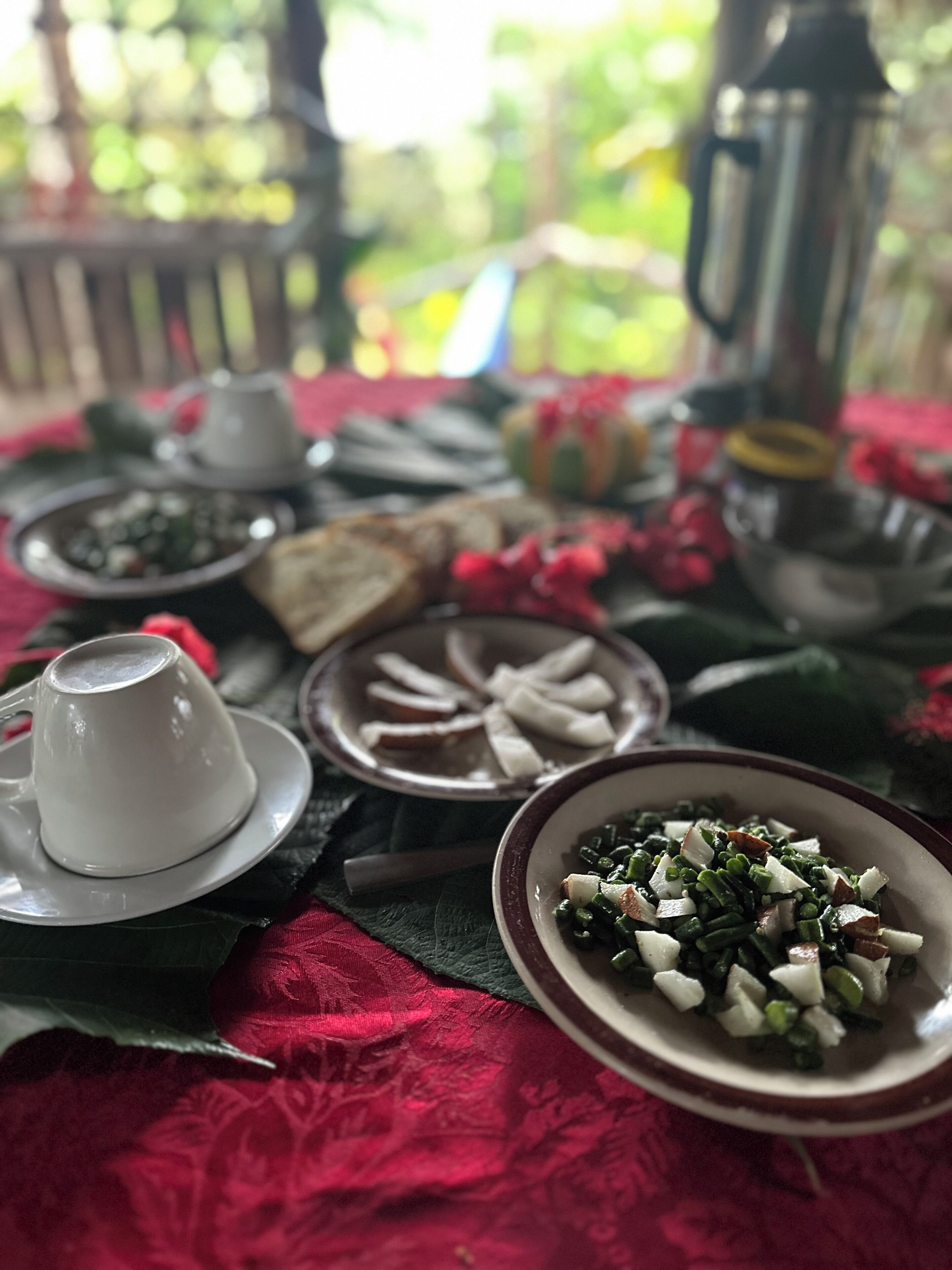 A table set with various dishes, including a bowl of green vegetables, a plate of sliced bread, and a cup of coffee.