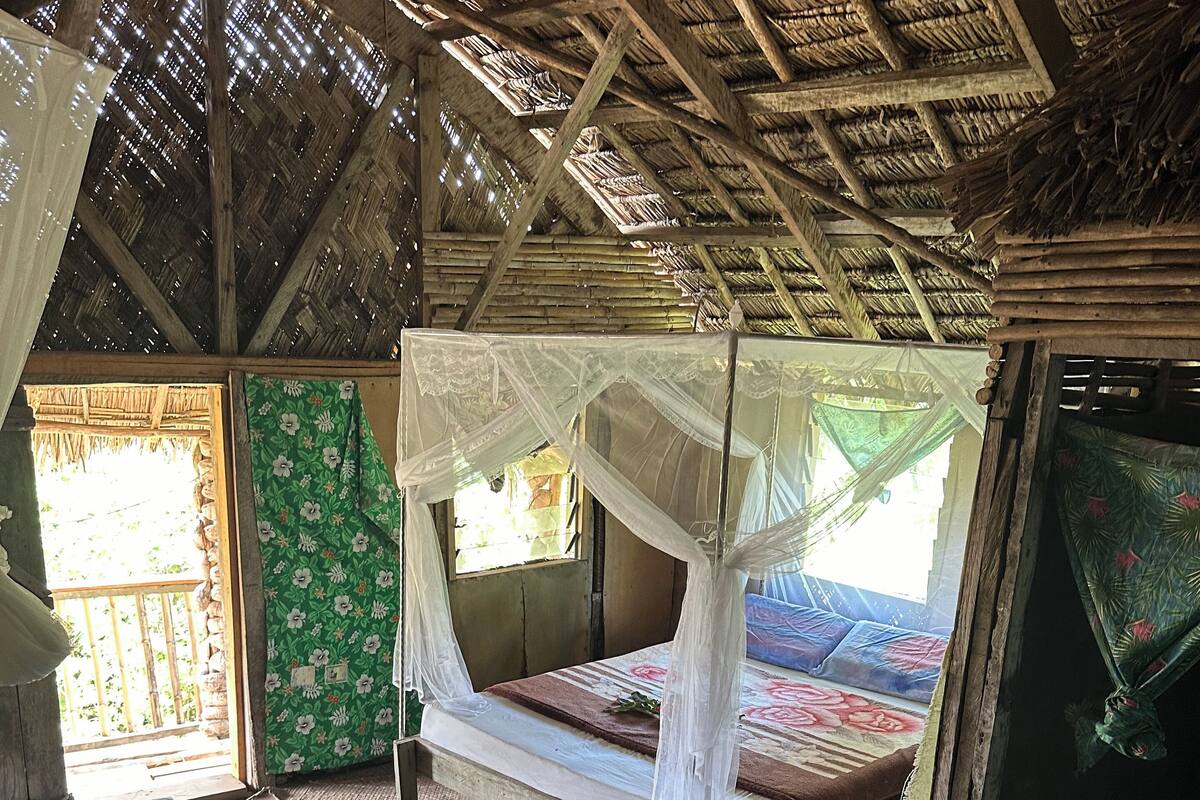 A rustic room with a thatched roof, wooden floors, and a bed with a canopy.