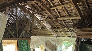 Una habitación rústica con techo de paja, pisos de madera y una cama con dosel.