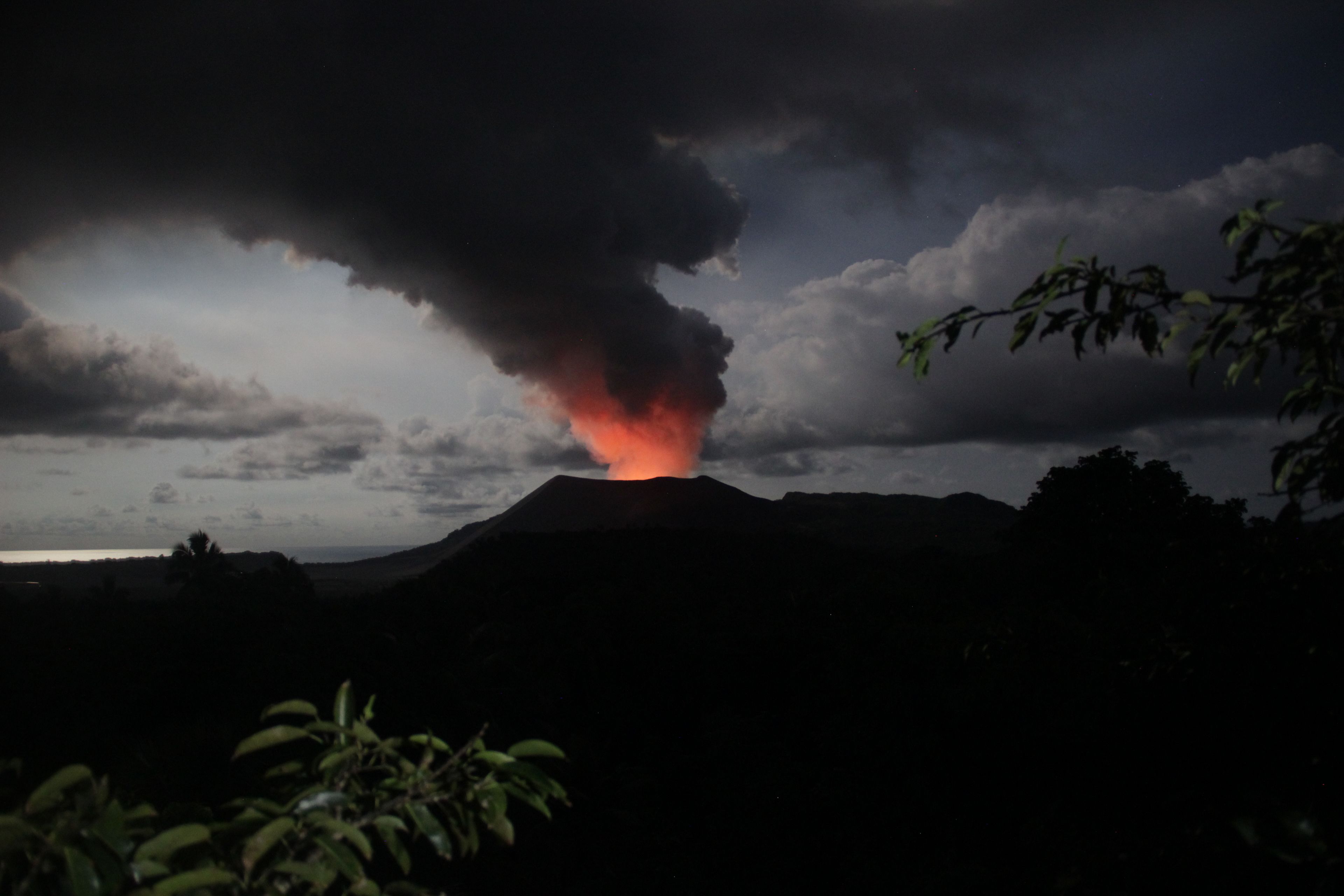 A volcano with a dark sky and a red glow at its peak.