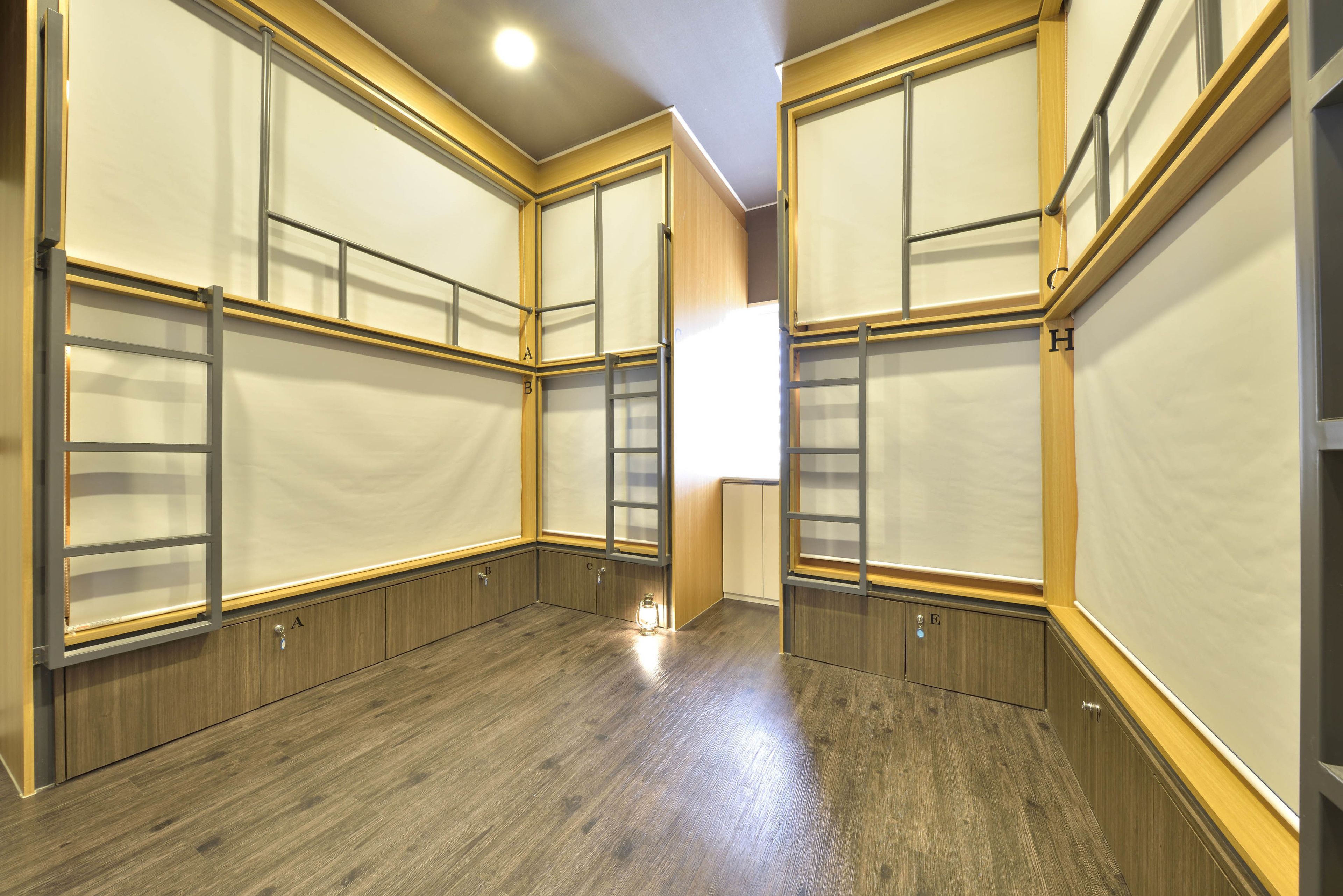 A hotel room with wooden flooring, built-in wardrobes, and a large window providing natural light.