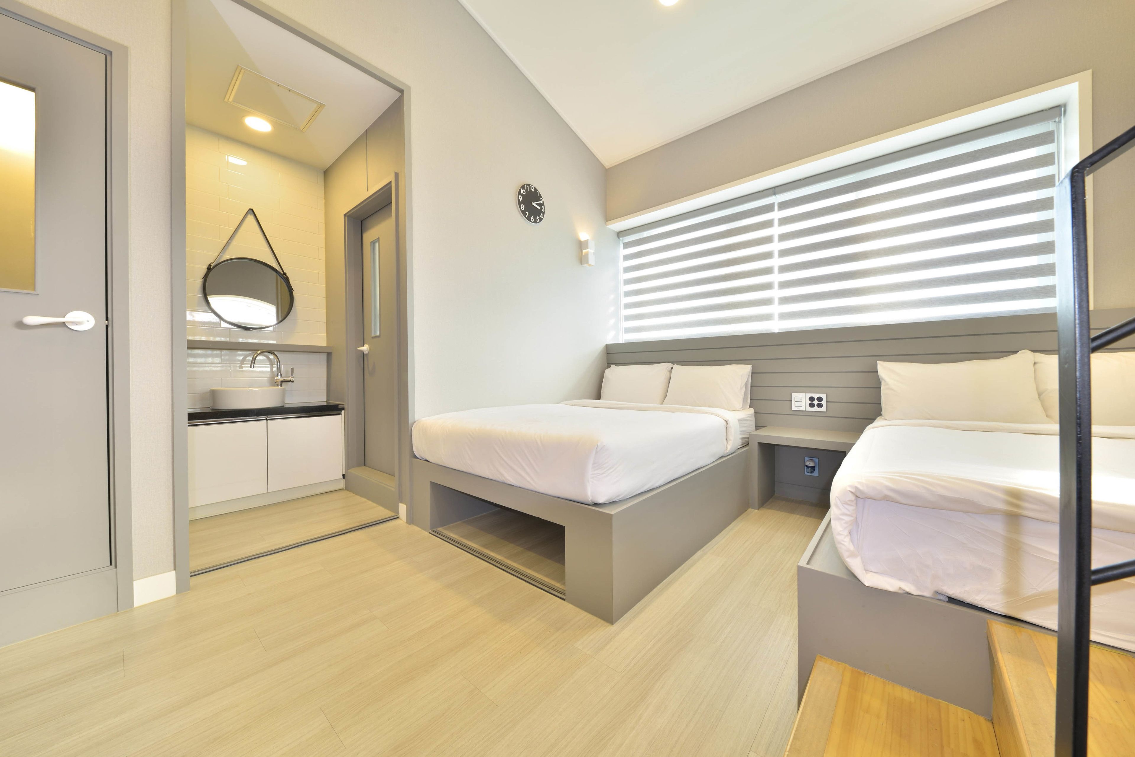 Une chambre moderne avec deux lits, un bureau intégré et une salle de bain équipée d’un miroir et d’un lavabo.