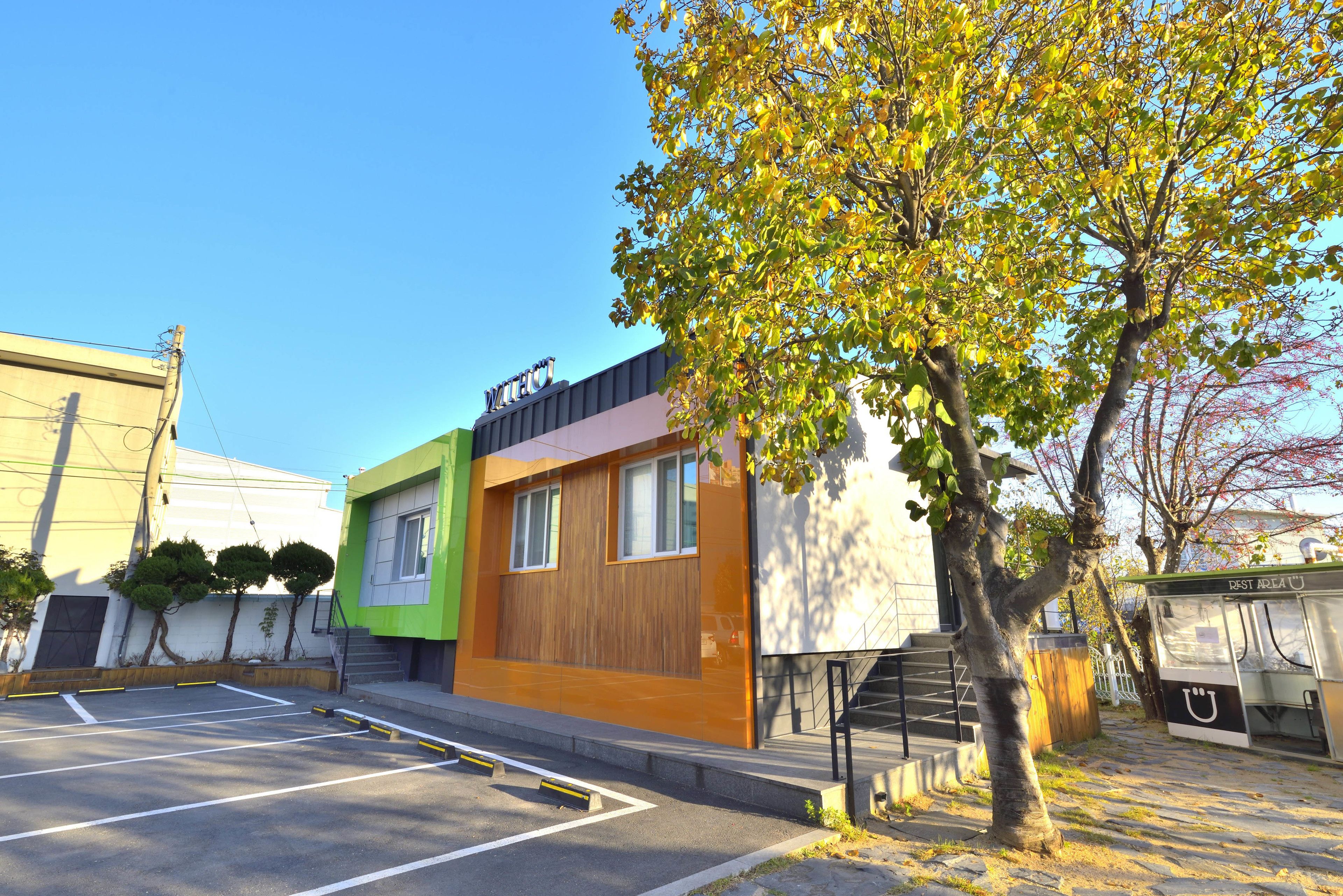 A modern building with a green and orange facade, a visible staircase, and a parking lot.