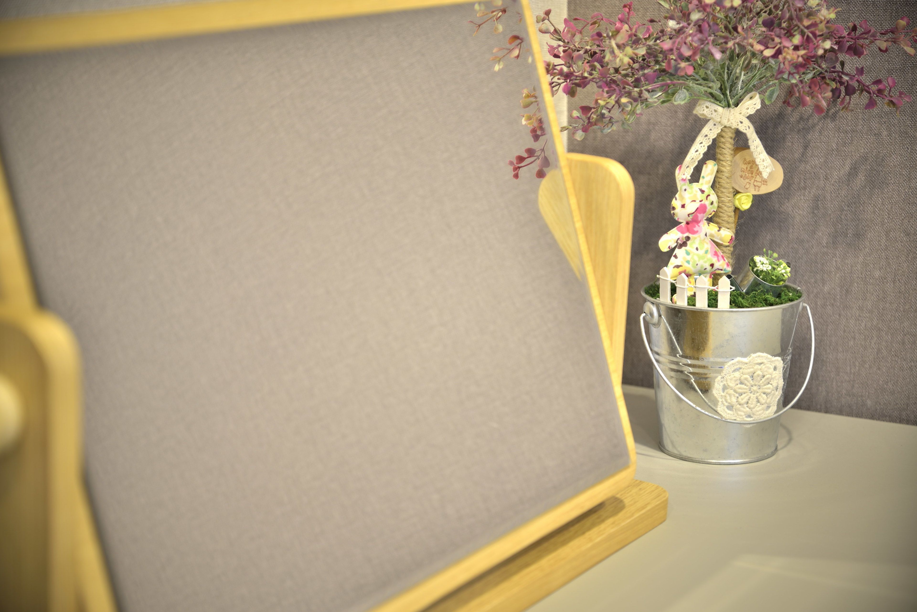 A framed picture with a wooden frame, a metal bucket with a decorative item, and a vase with flowers on a table.
