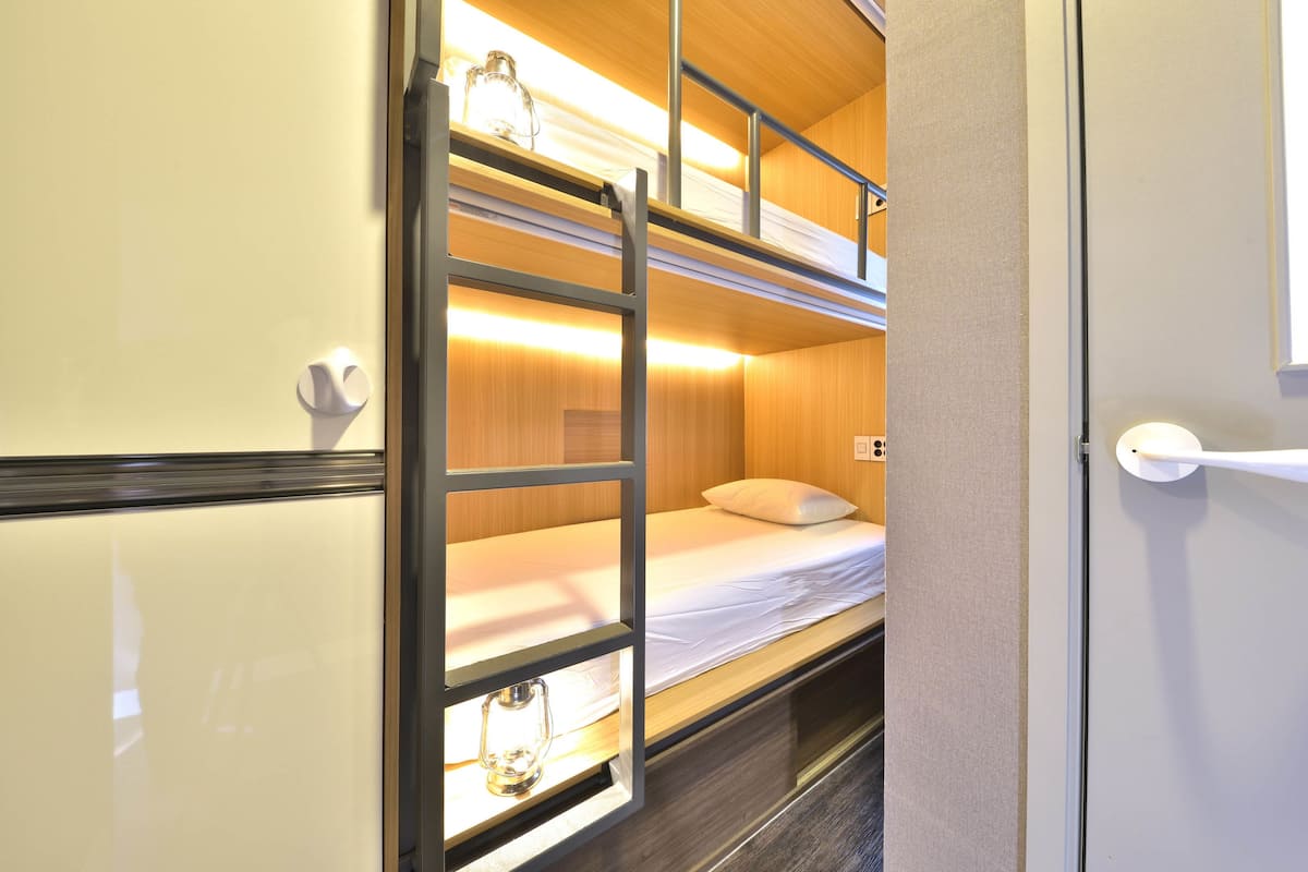 A bunk bed room with a ladder, a bedside table, and a window.