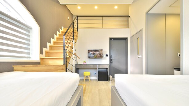 A modern hotel room with two beds, a wooden staircase, a desk, and a small stool. - WITH U Hotel & Guesthouse (Sokcho)