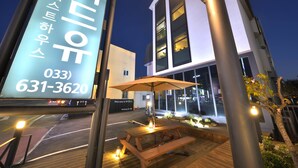 A modern building with a large illuminated sign, a wooden deck with a table and benches, and a well-lit entrance. - WITH U Hotel & Guesthouse (Sokcho)