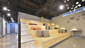 A modern interior with a wooden bench seating area, a staircase, and a metal table with items on it. - WITH U Hotel & Guesthouse (Sokcho)