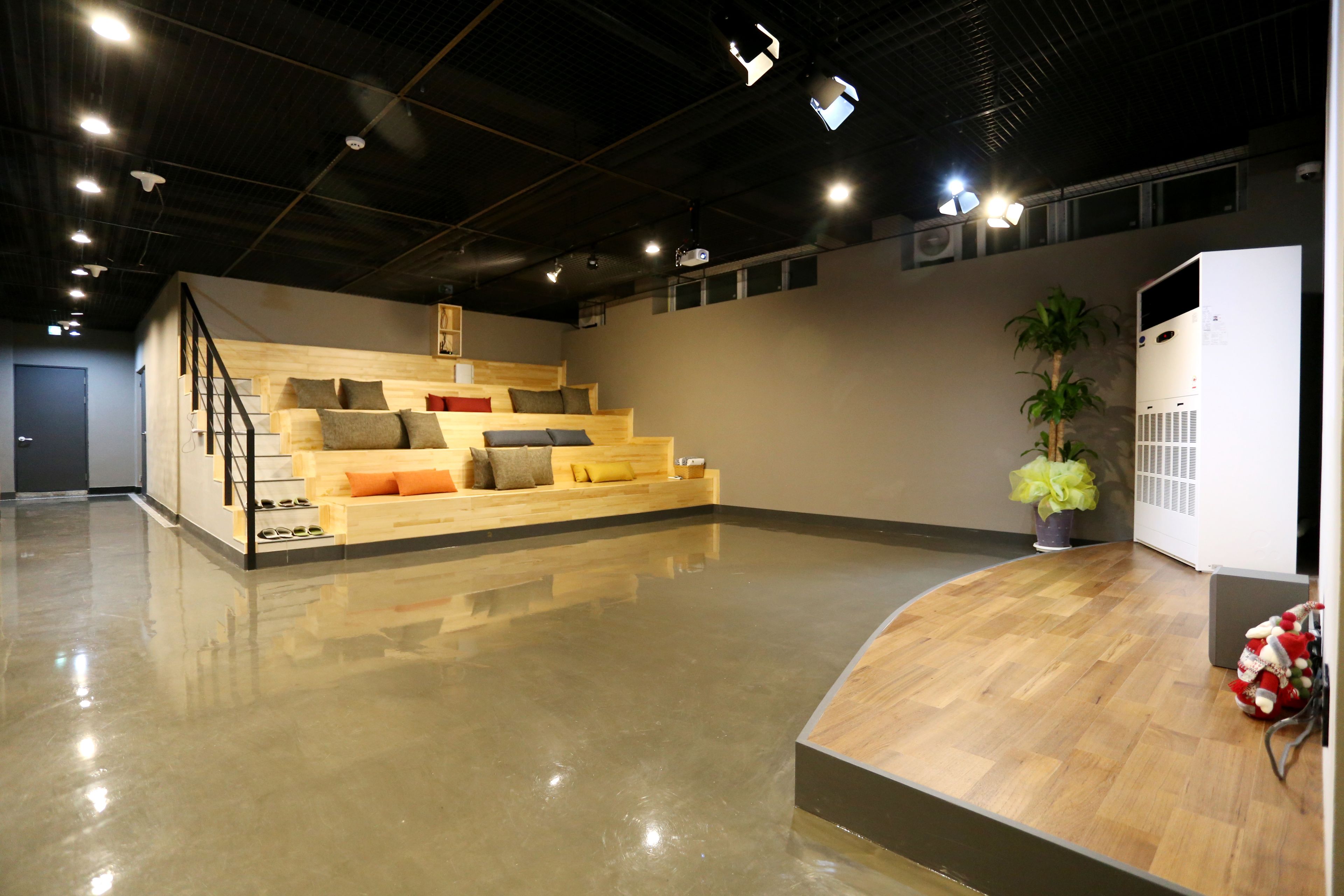 A spacious room with a polished floor, a wooden staircase with cushions, a potted plant, and a white air conditioning unit.