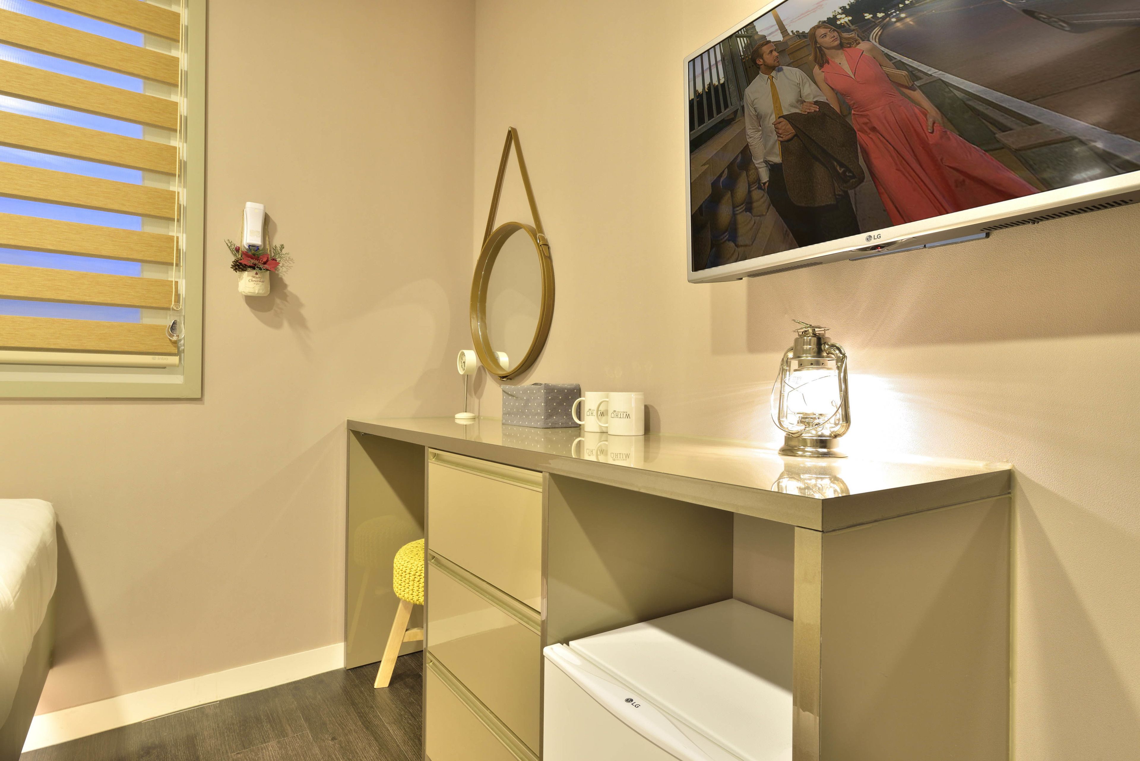 Hotelkamer met een bed, een bureau met spiegel, een televisie en een kleine koelkast.