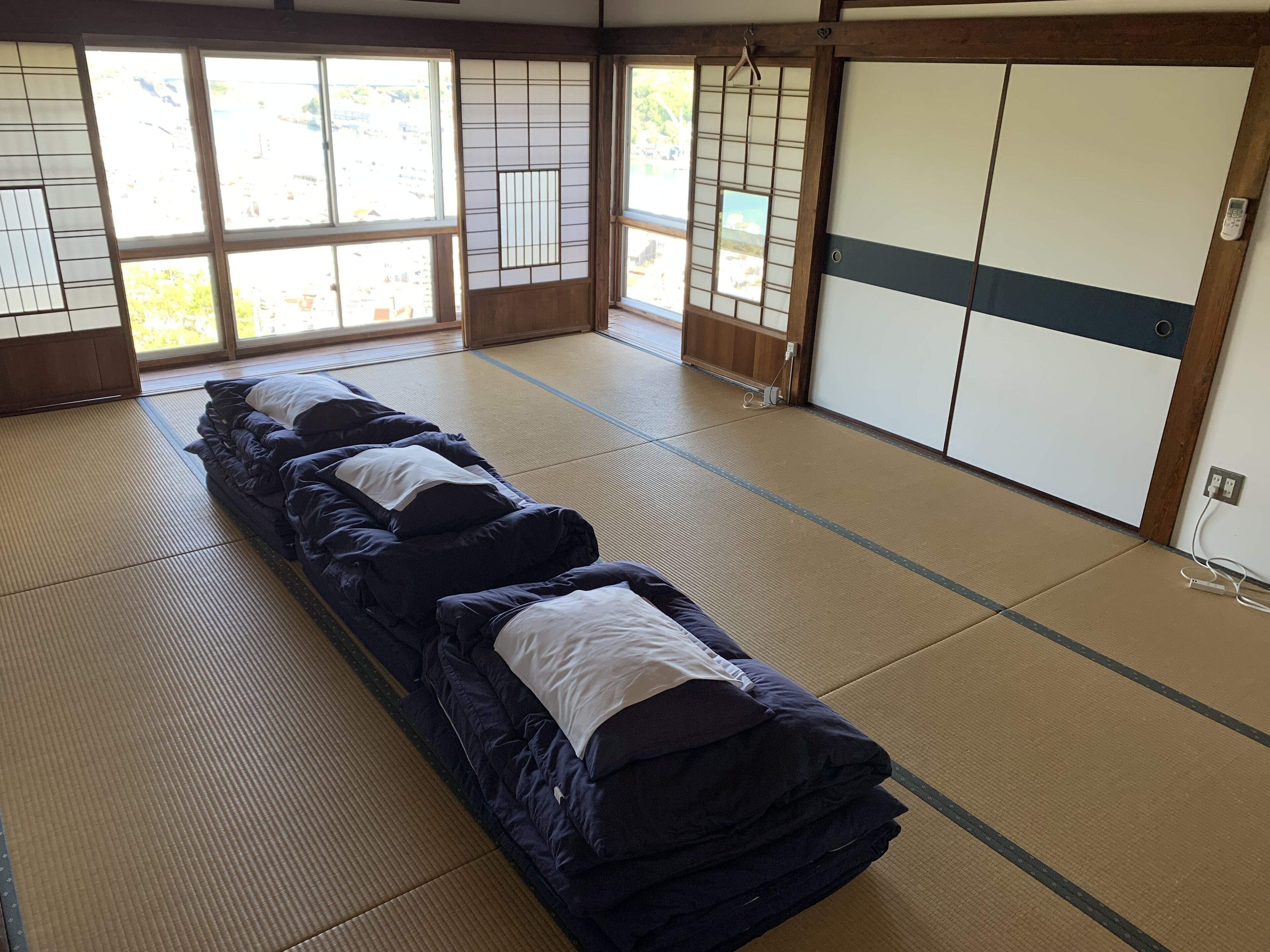 Tatami-mattoilla päällystetty huone, jossa on futon-patja, liukuovet ja näkymä ulos.