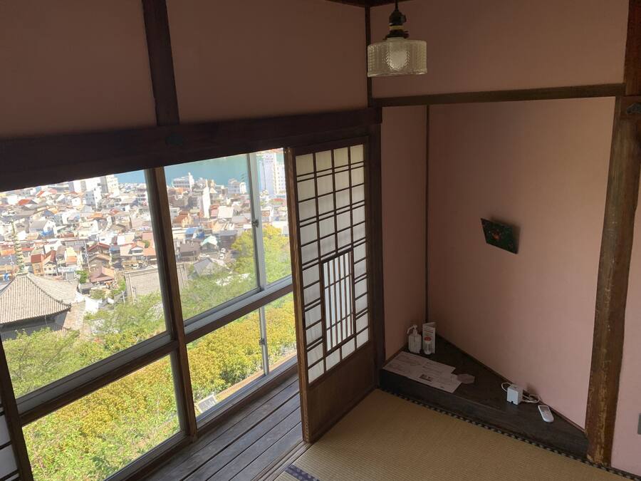 Ein traditioneller japanischer Raum mit Tatami-Böden, einem Shoji-Bildschirm und Blick auf eine Wohngegend.