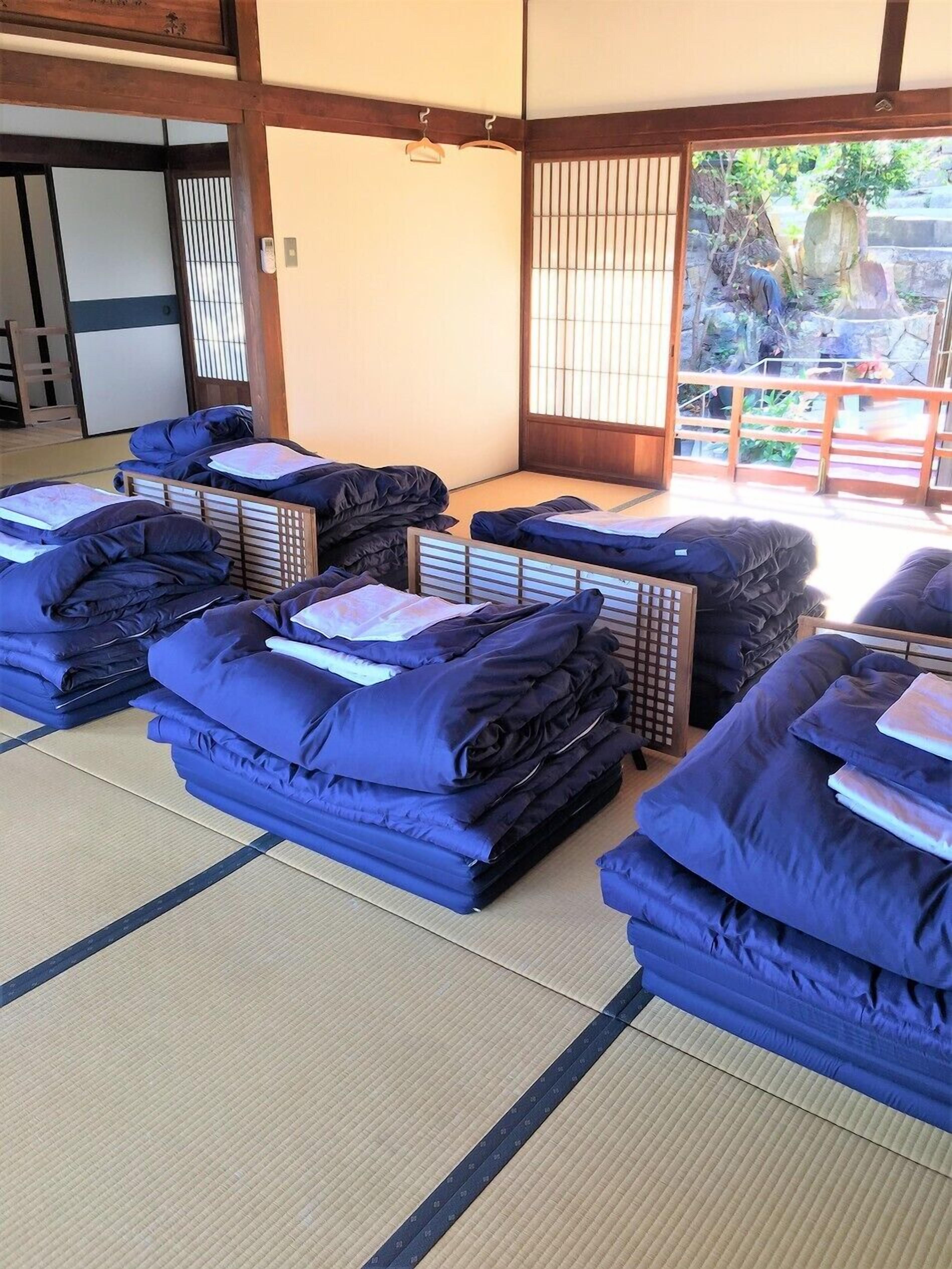 A traditional Japanese room with tatami flooring, multiple futon beds, and a view of a garden through a sliding door.