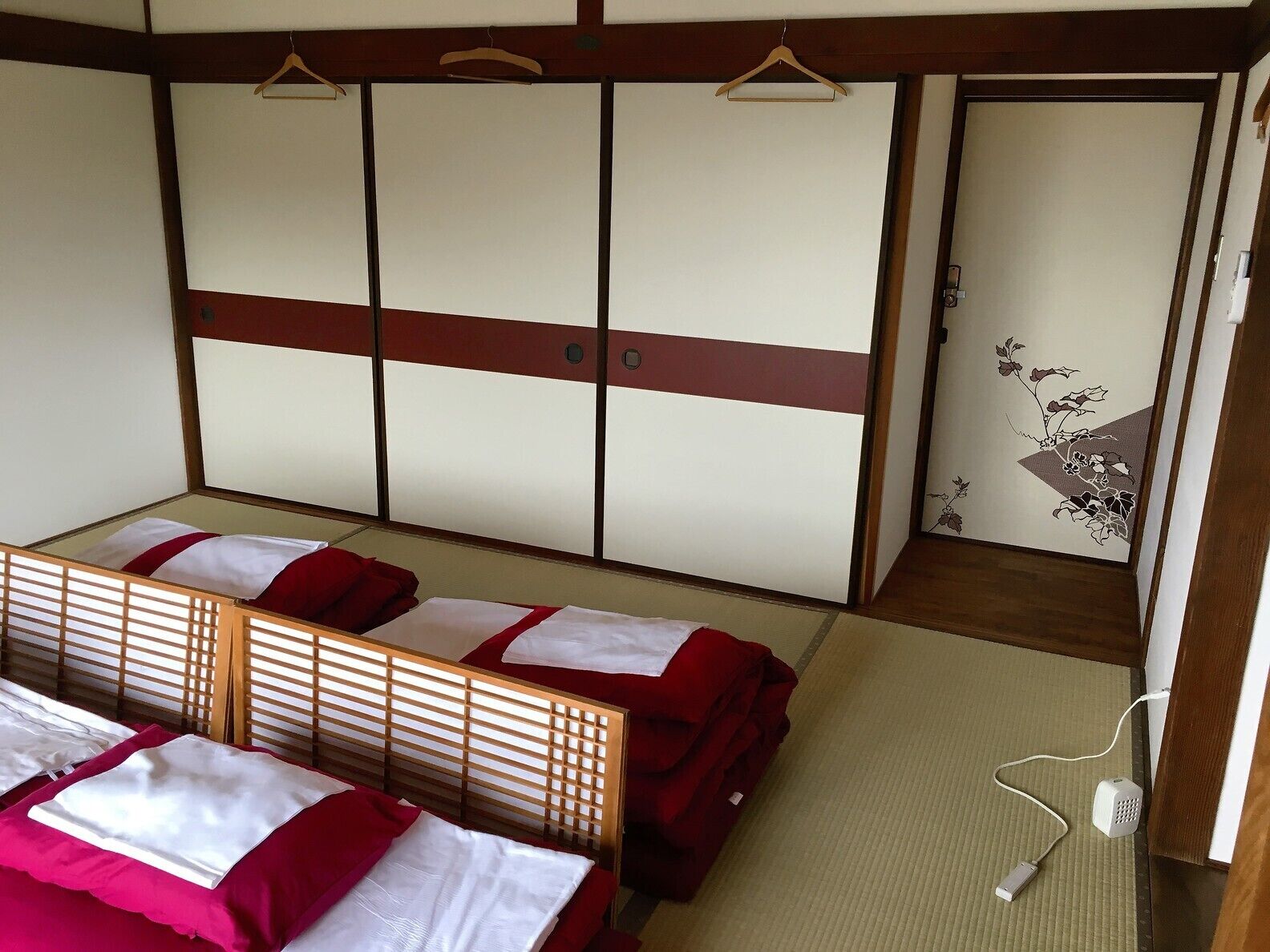 A traditional Japanese-style room with tatami flooring, a low wooden bed with red bedding, and a sliding shoji screen door.