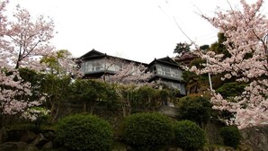 A traditional Japanese house with a stone wall and cherry blossoms. - Onomichi Guest House Miharashi-tei - Hostel (Onomichi)