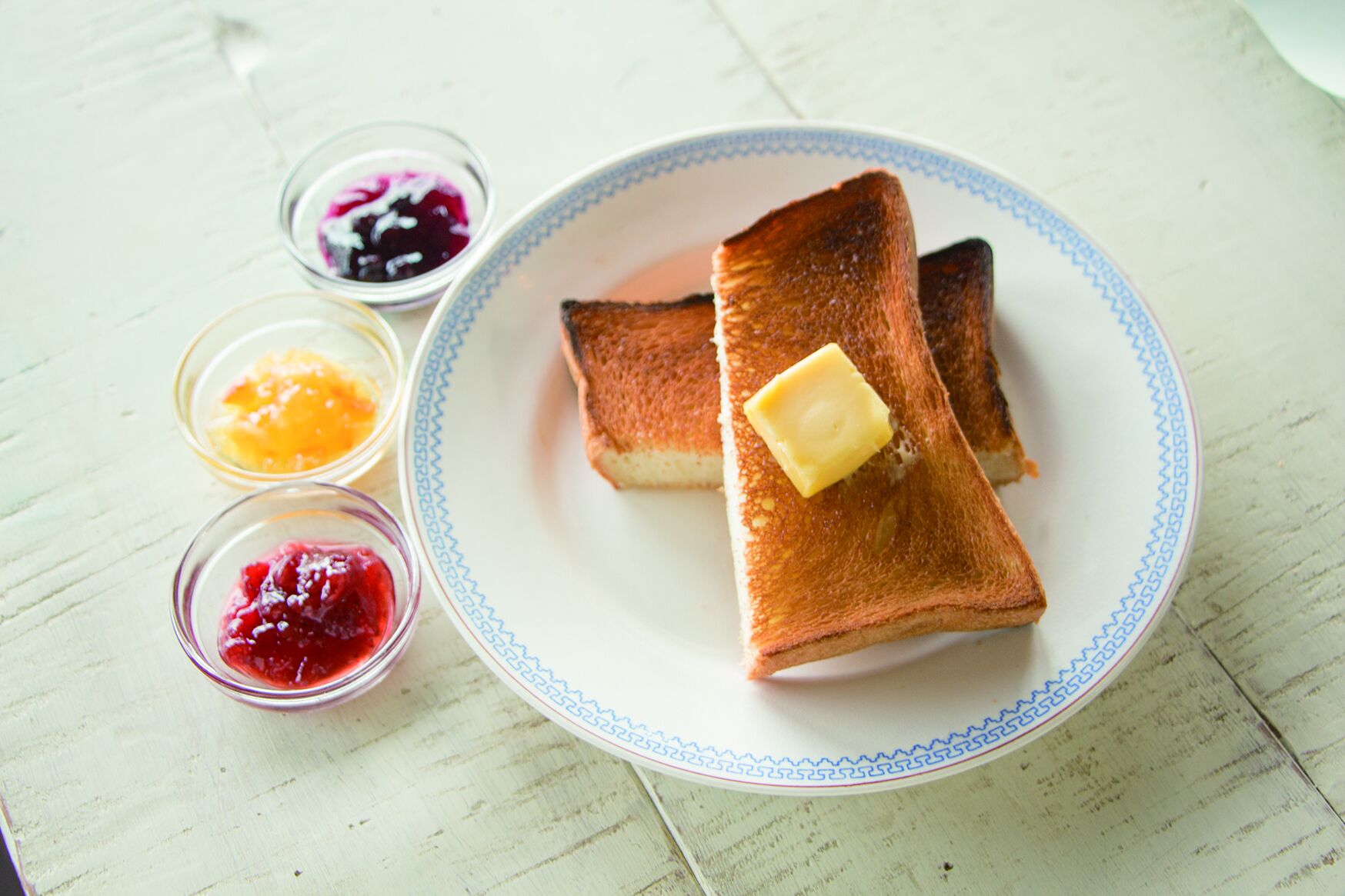 Ein Teller mit zwei Toastscheiben, Butter und drei kleinen Schälchen Marmelade.
