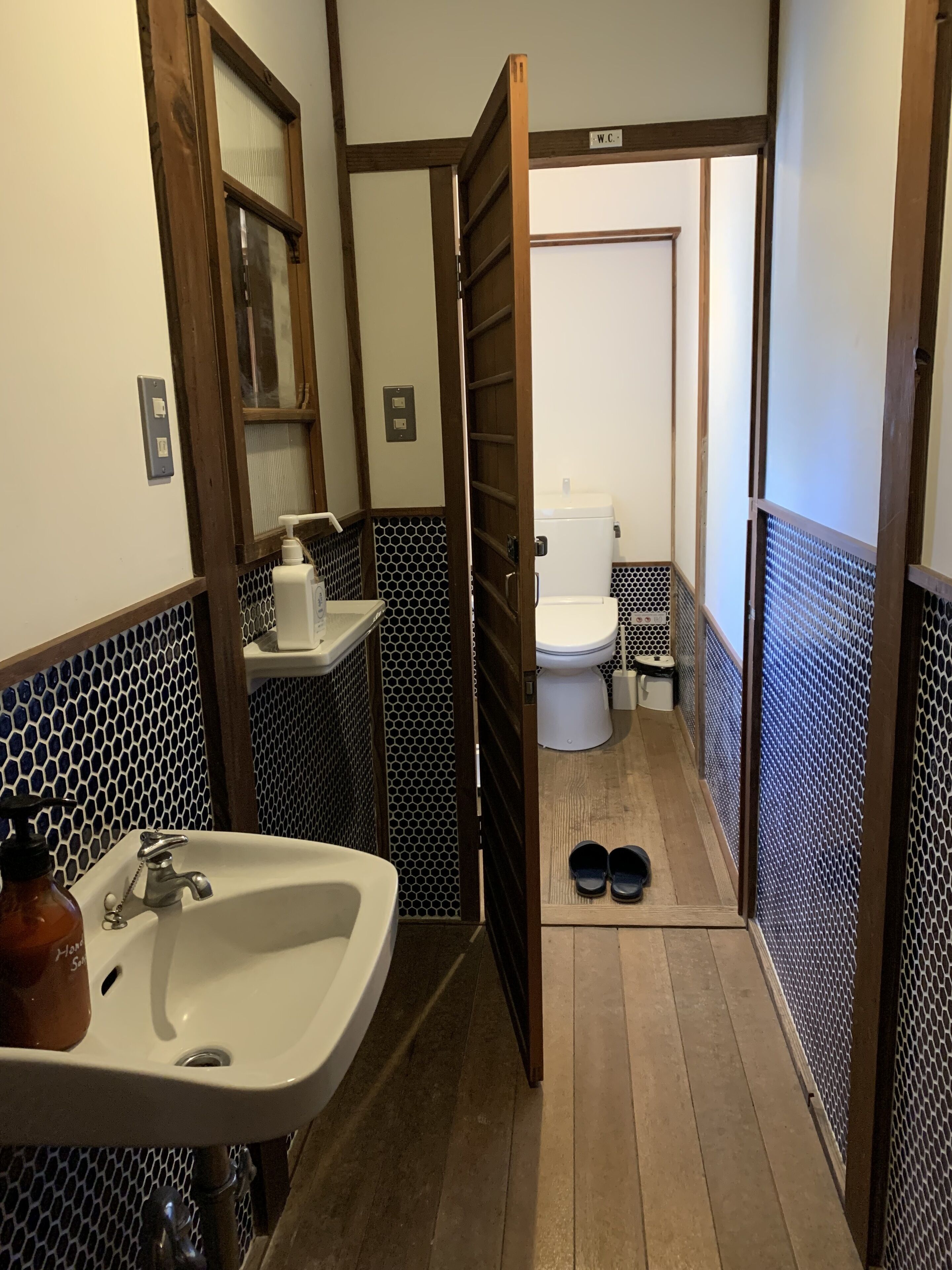 Une petite salle de bain avec un lavabo, des toilettes et une paire de chaussures posées sur le sol.