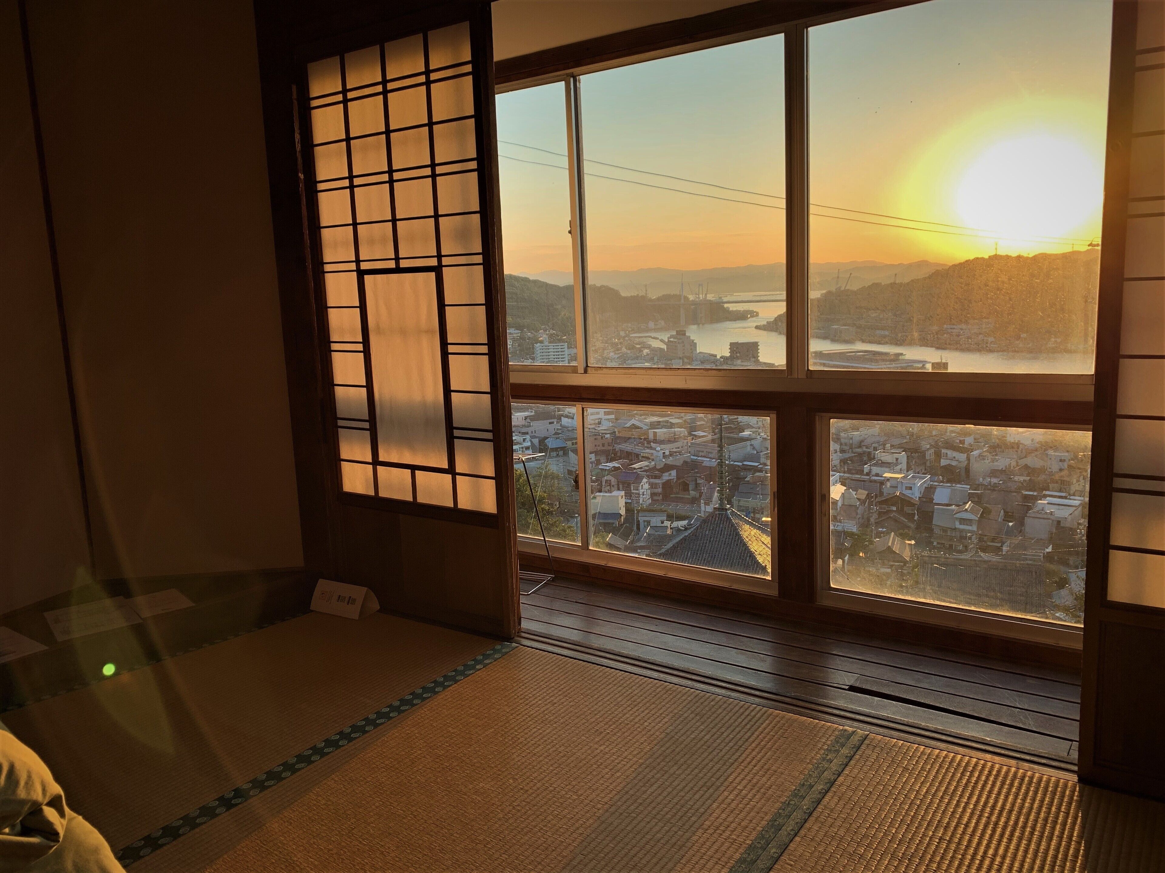 Een traditionele Japanse kamer met tatami vloerbedekking, een shoji schuifwand en uitzicht op een stadslandschap bij zonsondergang.