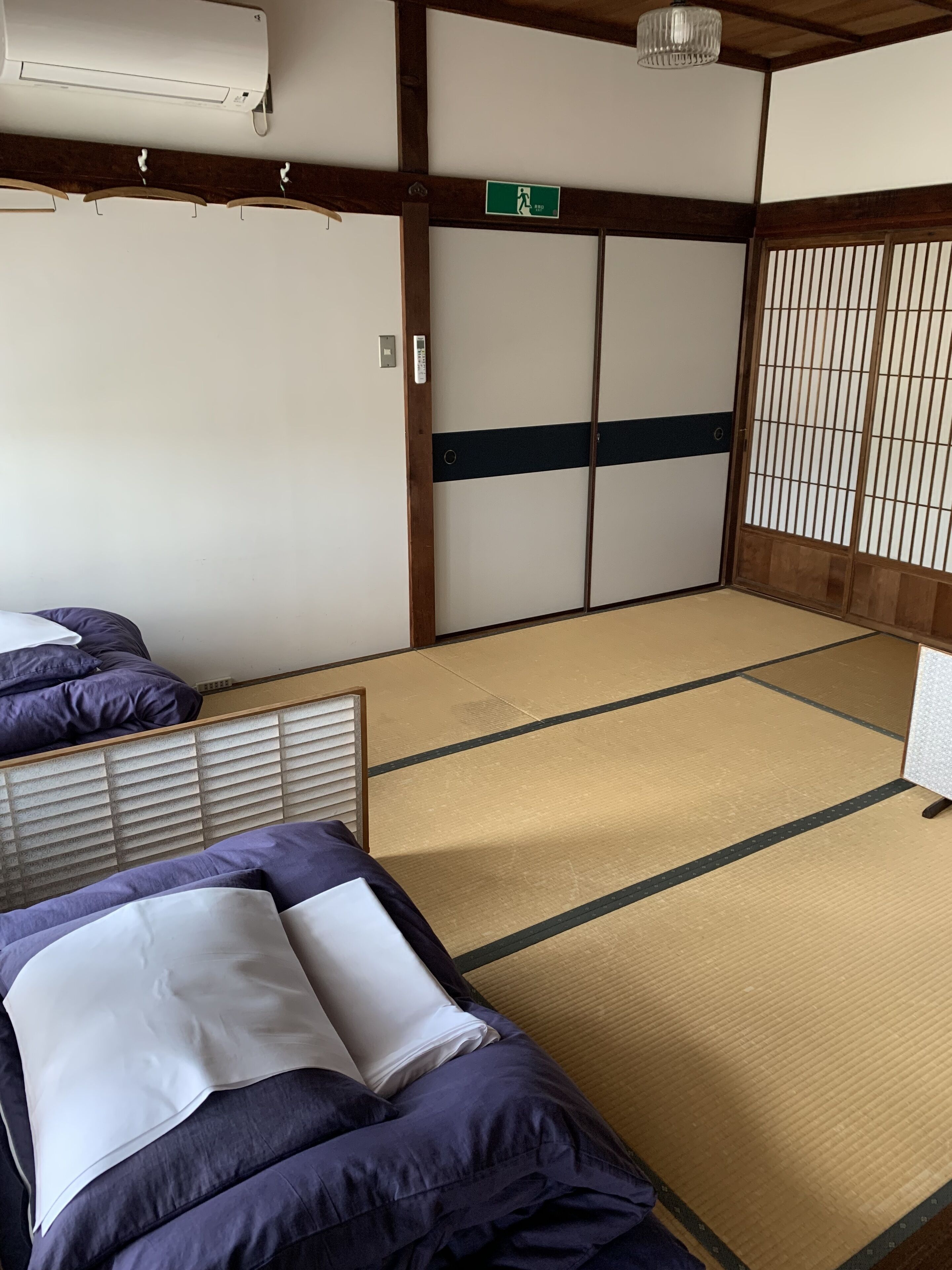 A traditional Japanese room with tatami flooring, a shoji screen door, and a bed with purple bedding.