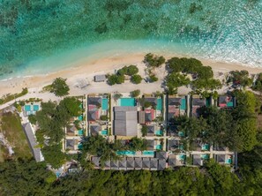 An aerial view of a coastal resort with multiple buildings, some with green roofs, and a sandy beach adjacent to the ocean.