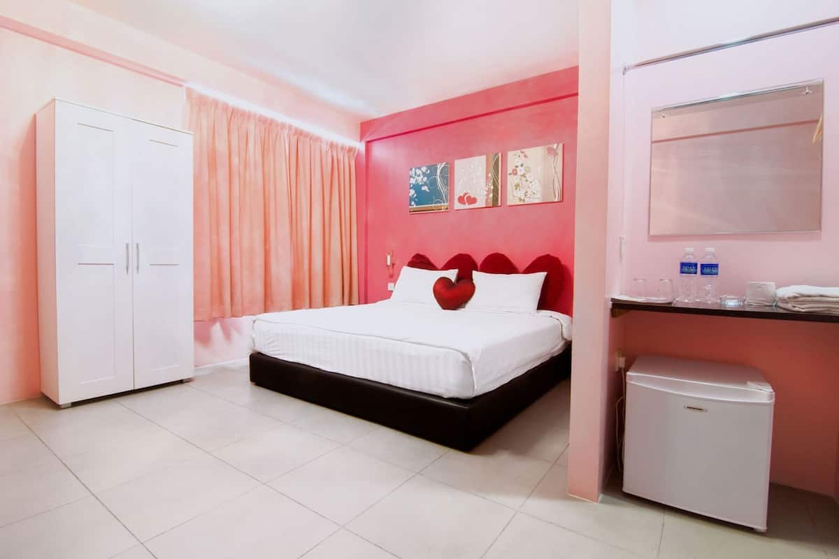 A bedroom with a bed, a wardrobe, a small fridge, and a vanity with toiletries.