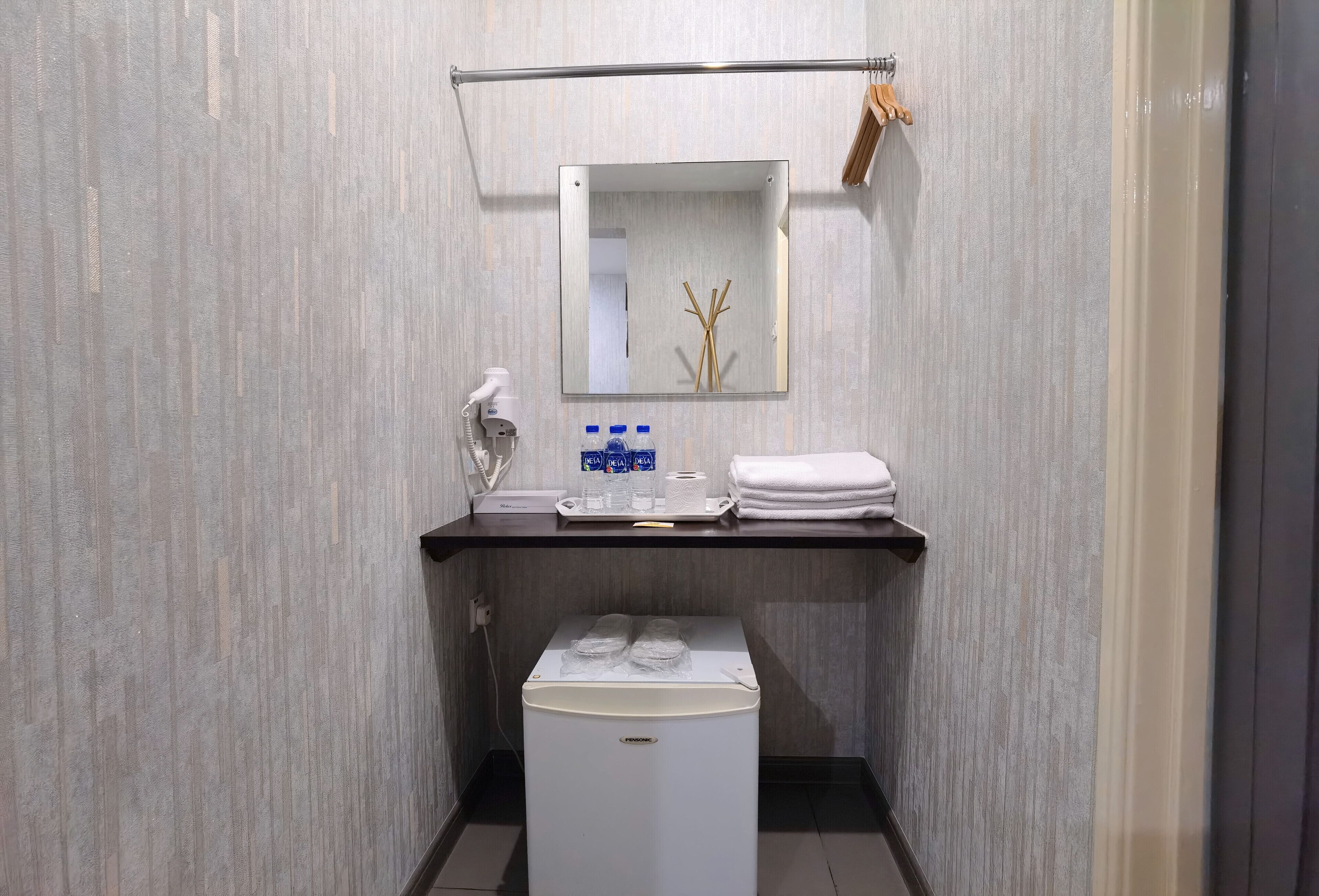 Een kleine badkamer met spiegel, handdoekhouder en een kleine koelkast.