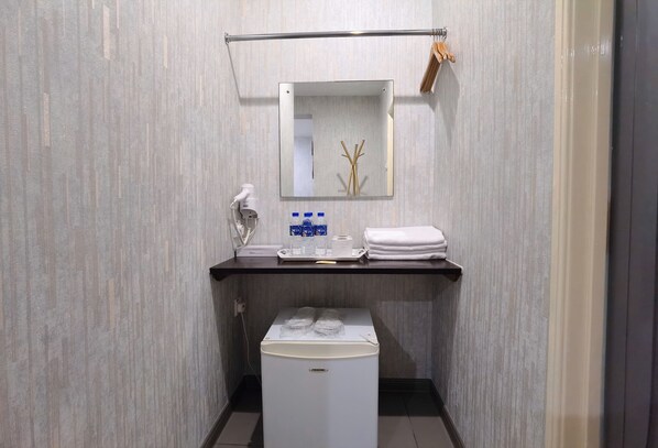 Un baño pequeño con espejo, toallero y un refrigerador compacto.