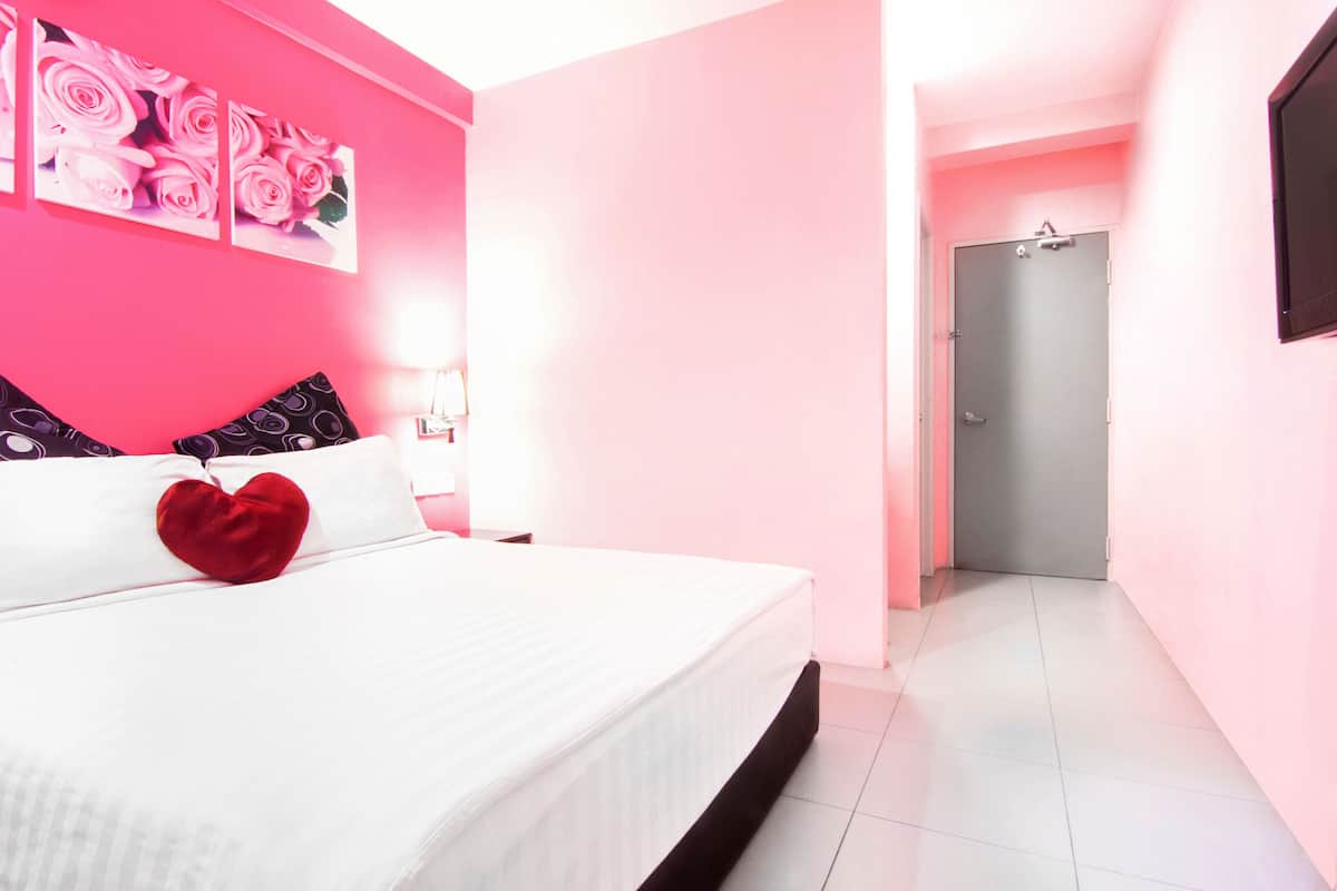 A bedroom with a bed, a heart-shaped pillow, and a wall with pink roses.