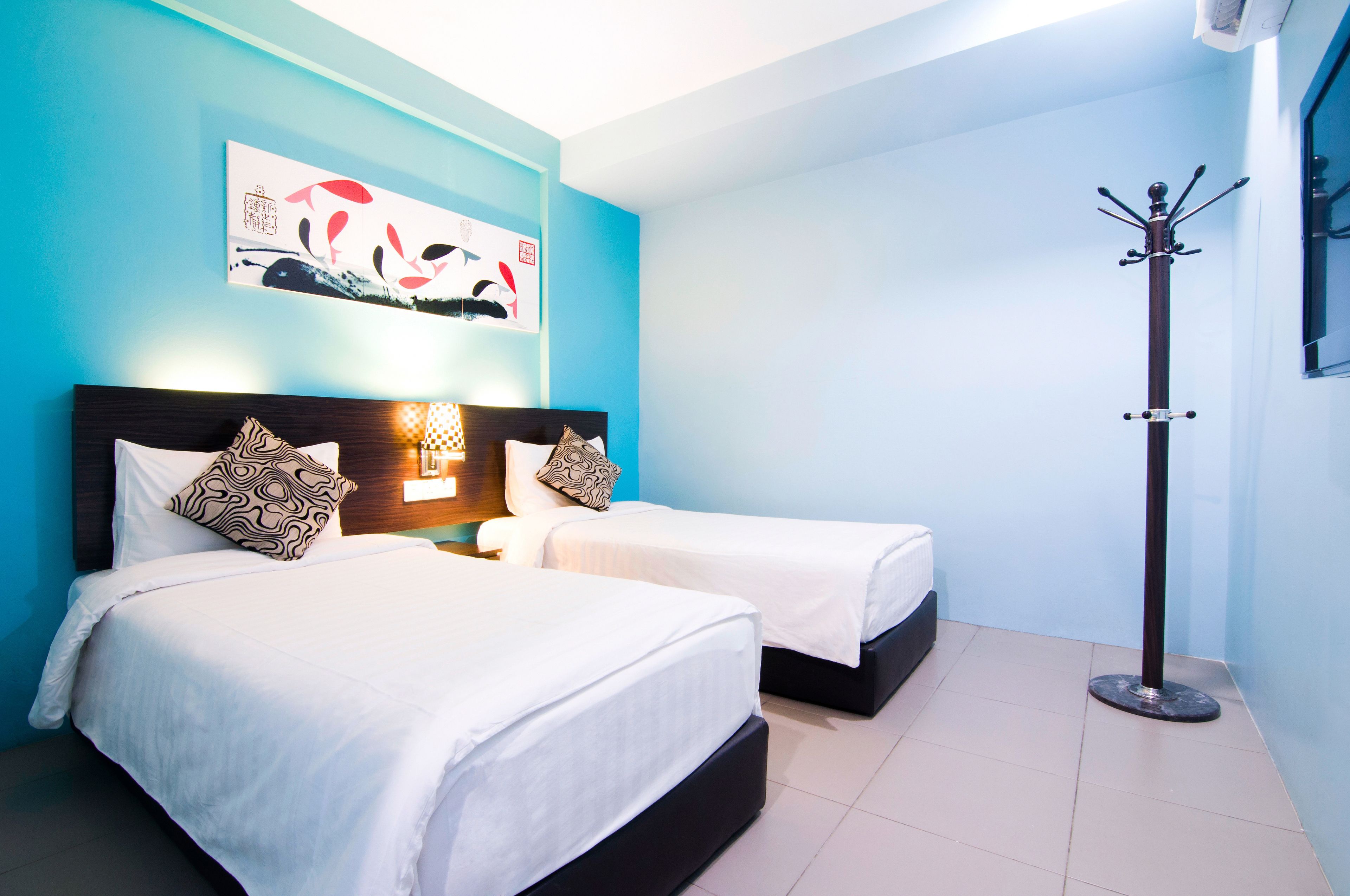 Ein Hotelzimmer mit zwei Betten, einem Nachttisch, einem Wandbild und einem Kleiderständer.
