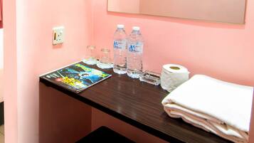A bathroom counter with a magazine, two water bottles, a roll of toilet paper, and a stack of towels.