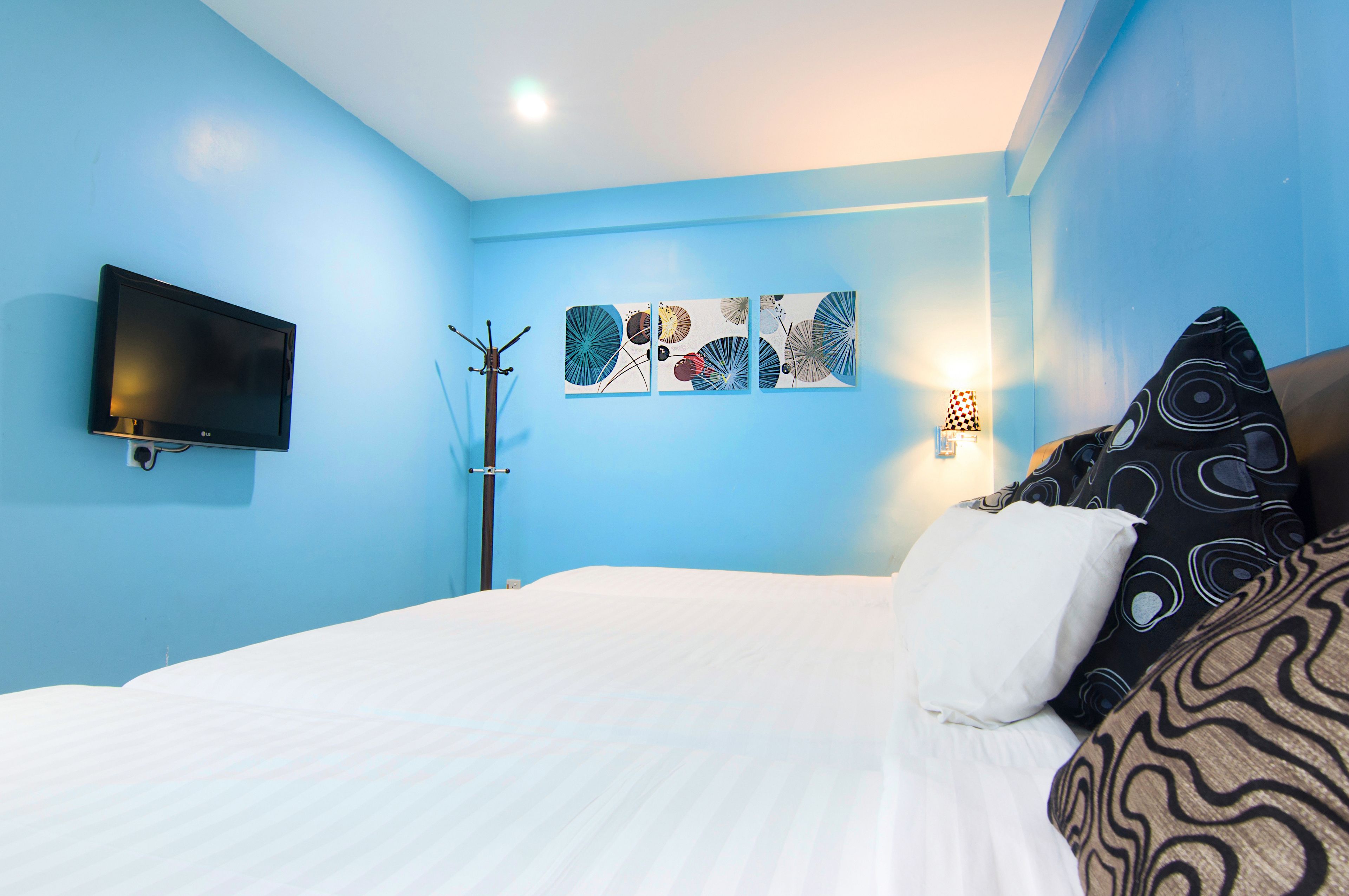 Habitación de hotel con una cama, un televisor de pantalla plana, una obra de arte en la pared y un perchero.