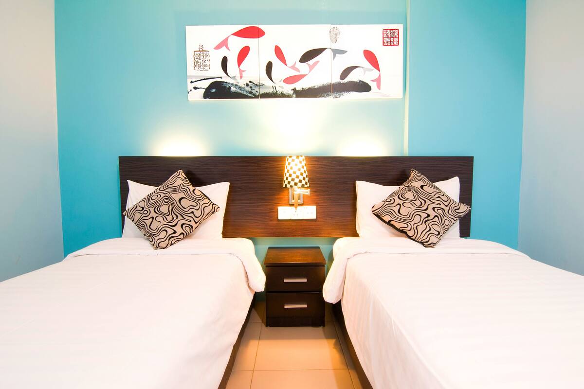 A hotel room with two beds, a nightstand with a lamp, and a wall-mounted artwork.