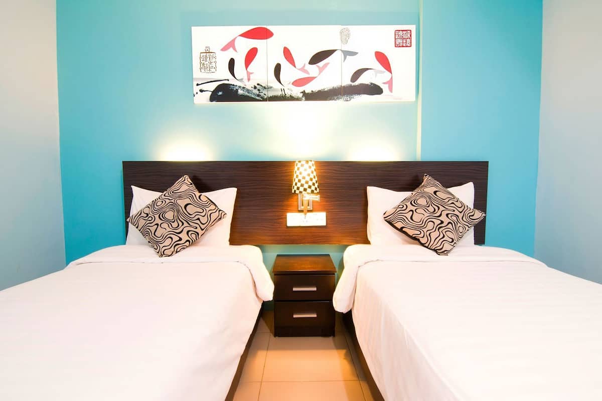 A double bed with patterned pillows, a nightstand with a lamp, and a wall-mounted artwork above the bed.