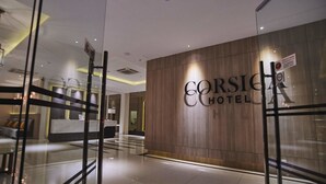 A modern hotel lobby with a reception desk, a wooden wall with the hotel name, and a glass partition. - Corsica Hotel (Kulai)