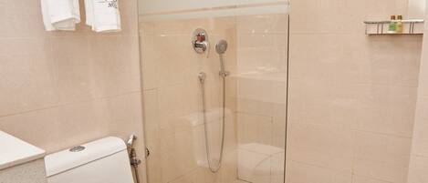 Une salle de bain moderne avec une douche à parois de verre, des toilettes avec un porte-serviettes et une étagère contenant des articles de toilette.
