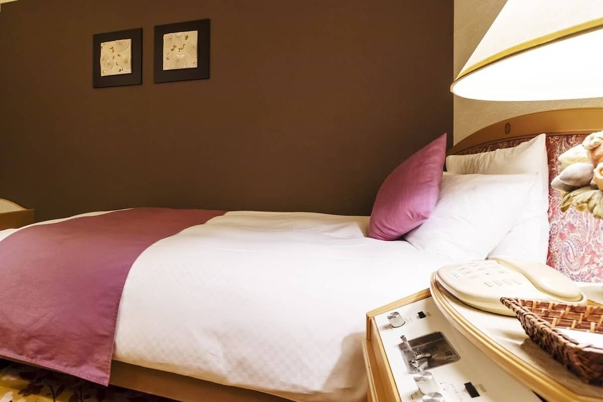 Una habitación de hotel con cama, mesita de noche, lámpara y teléfono.