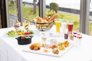 En frukostbuffé med ett varierat utbud av rätter och drycker, och en vacker utsikt genom fönstret.