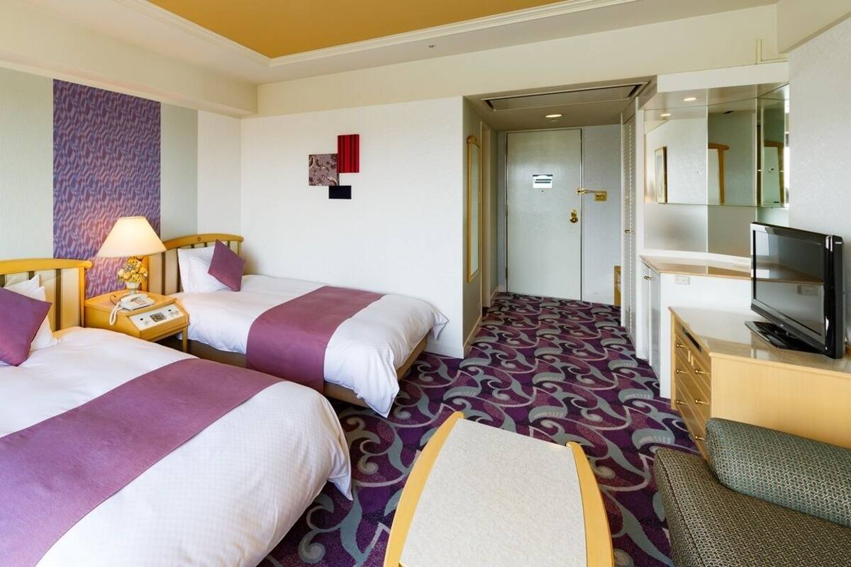 Habitación de hotel con dos camas, televisión, escritorio y puerta al baño.