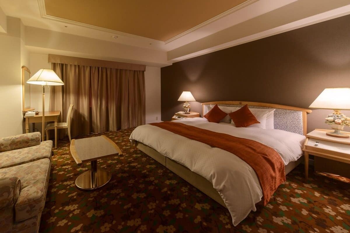 Una habitación de hotel con cama, una silla, una mesita y una lámpara.