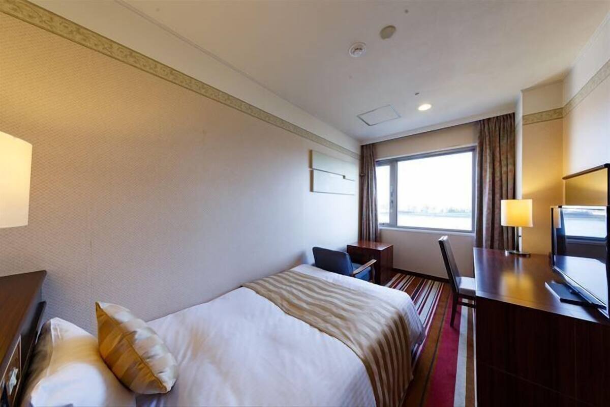 Una habitación de hotel con una cama, un escritorio con computadora, televisión y ventana con cortinas.