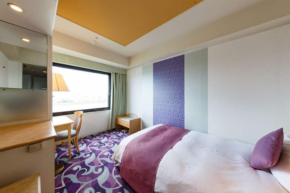 Una habitación de hotel con cama, escritorio, silla y ventana con cortinas.
