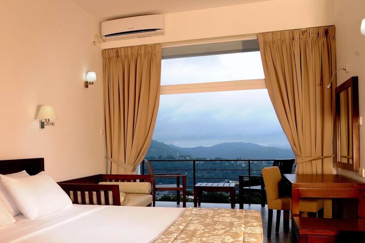 A hotel room with a bed, a desk, a chair, and a view of mountains through large windows.