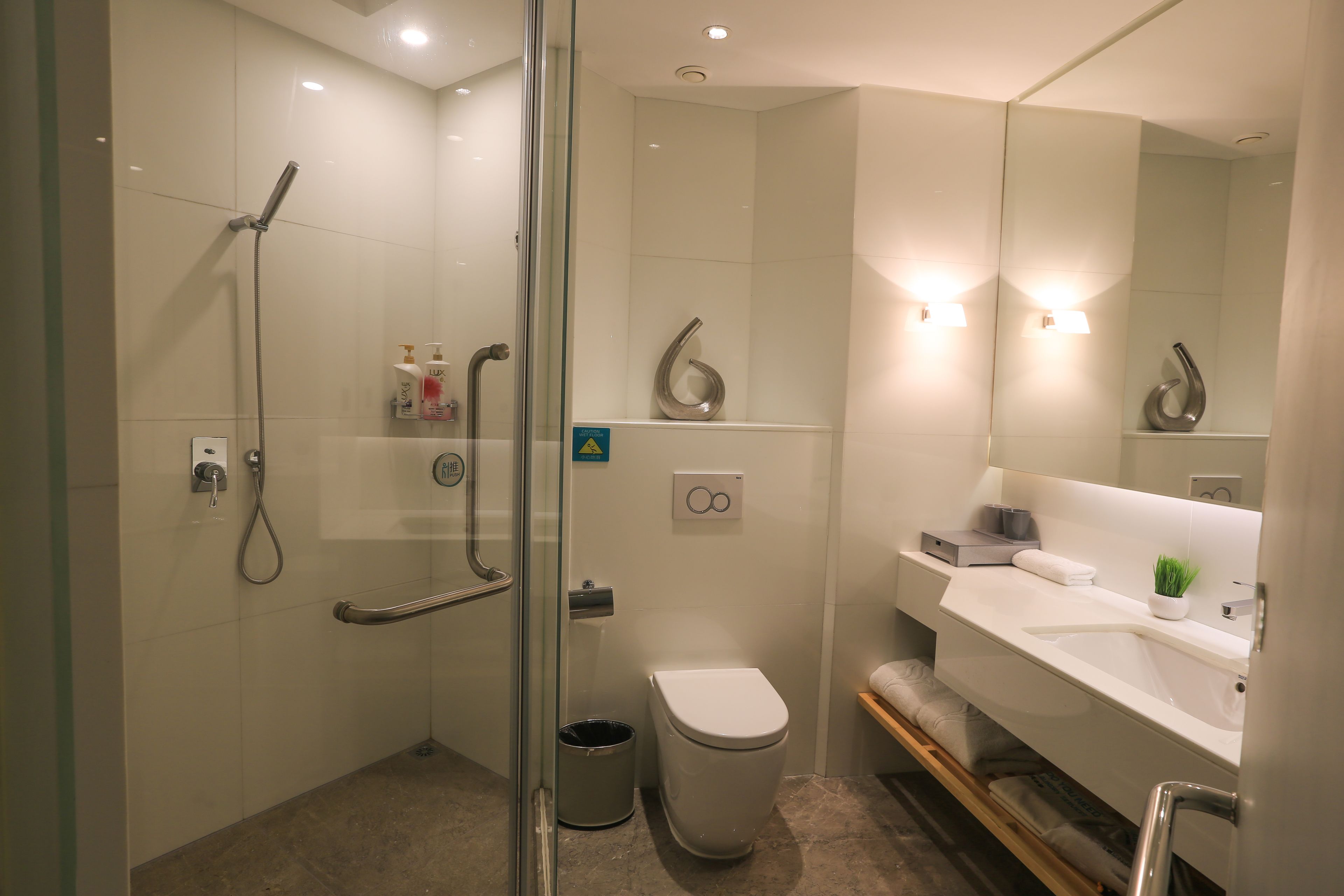 Ein modernes Badezimmer mit einer Duschkabine aus Glas, einer Toilette, einem Waschbecken mit Spiegel und einer kleinen Pflanze auf der Ablagefläche.