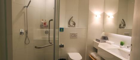 A modern bathroom with a glass shower enclosure, a toilet, a sink with a mirror, and a small plant on the countertop.
