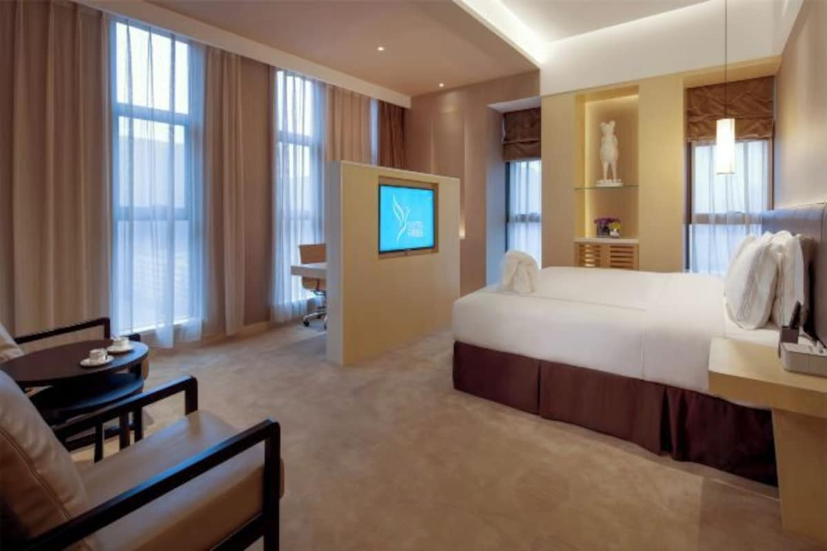 A hotel room with a bed, a desk, a chair, a TV, and a large window.
