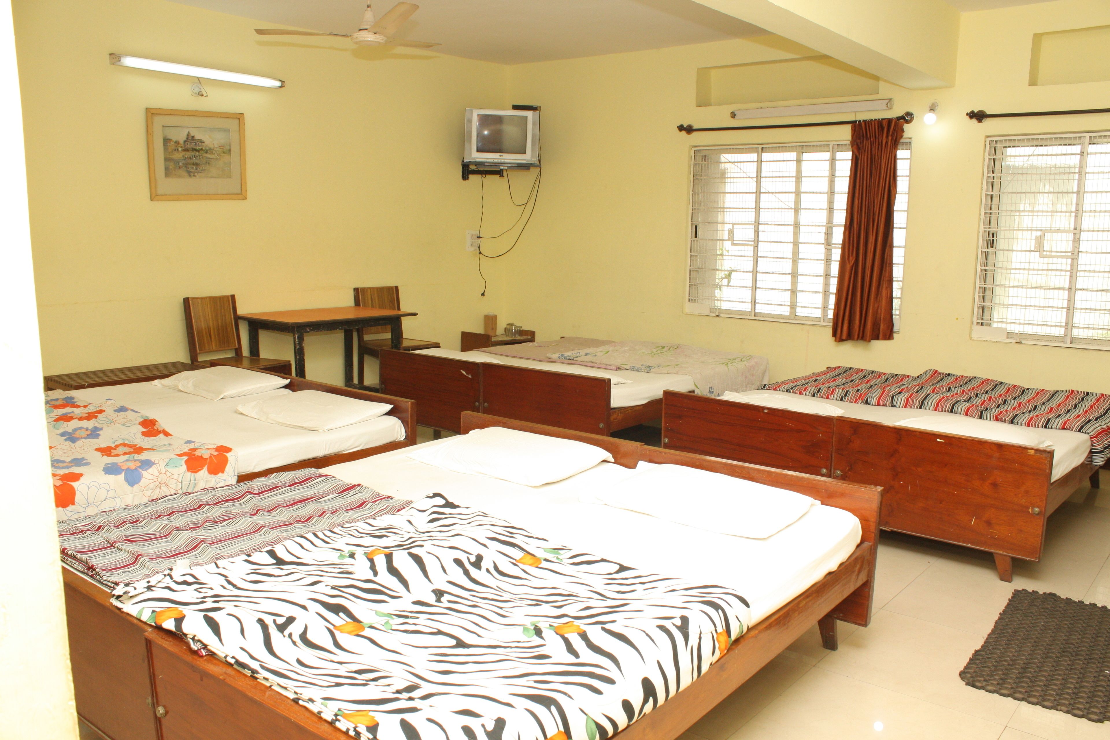 A hotel room with two beds, a desk, a chair, a television, and windows with curtains.