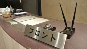 Un comptoir d’accueil d’hôtel avec une plaque nominative, un écran d’ordinateur, un clavier, un téléphone et un petit panier contenant divers objets.