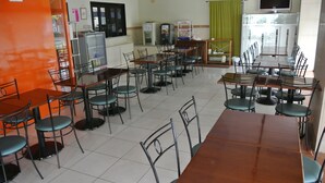 Un espace repas avec plusieurs tables et chaises, un réfrigérateur, un distributeur automatique et un téléviseur fixé au mur.