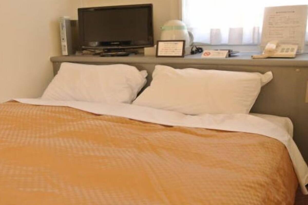 Ett hotellrum med en säng, en tv, en vattenkokare och en telefon på ett nattduksbord.