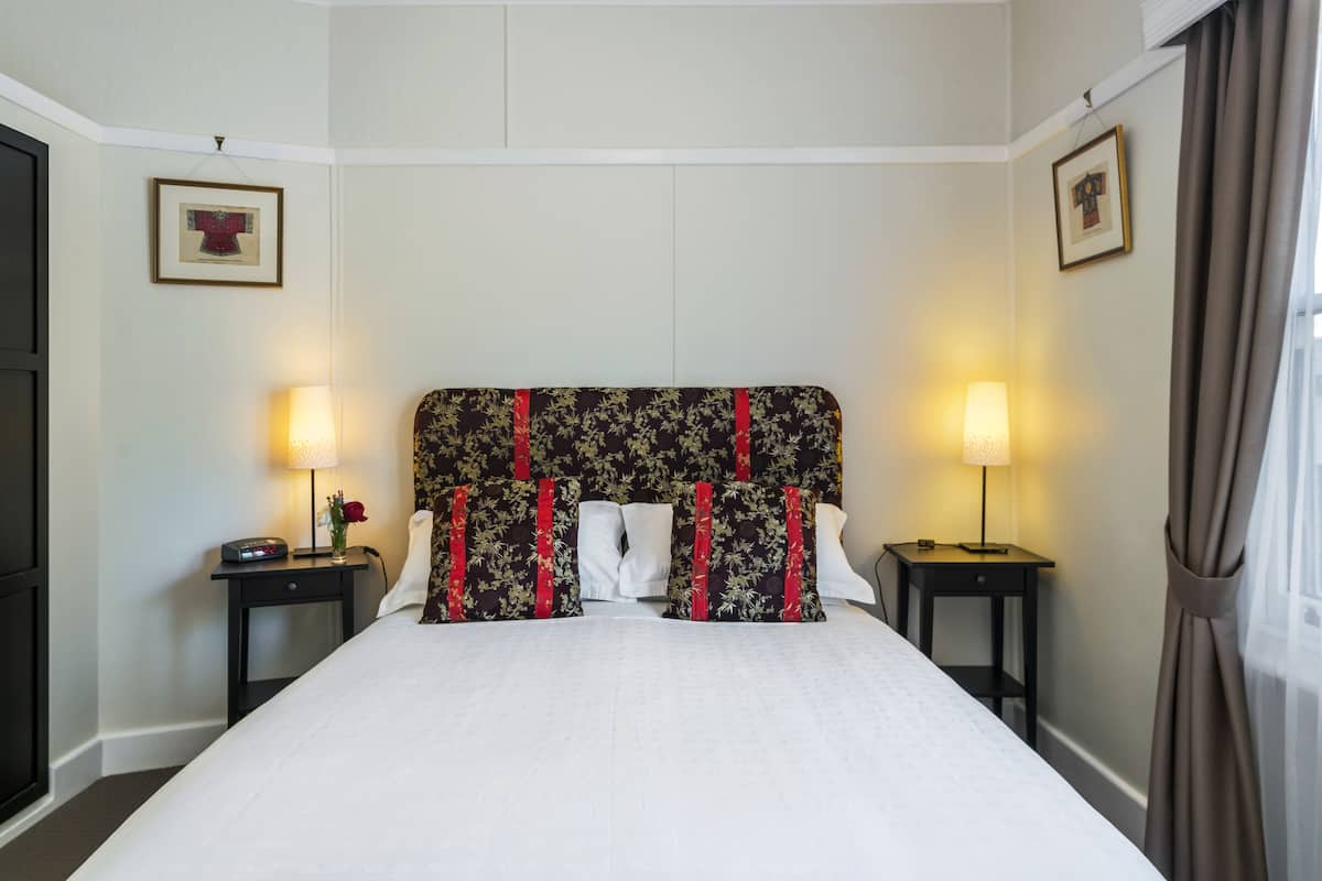 A neatly made bed with a floral headboard, two bedside tables with lamps, and framed pictures on the walls.